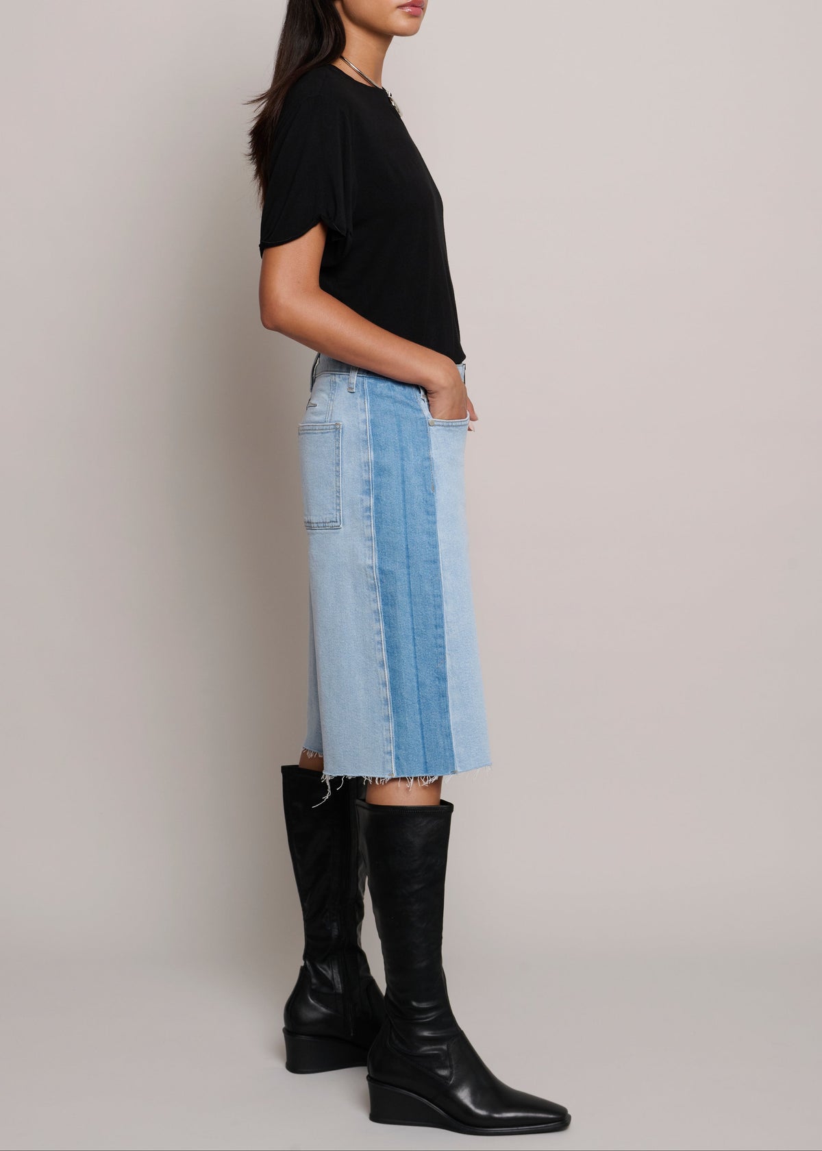Woman wearing a black top and denim skirt with black knee-high boots on a plain background