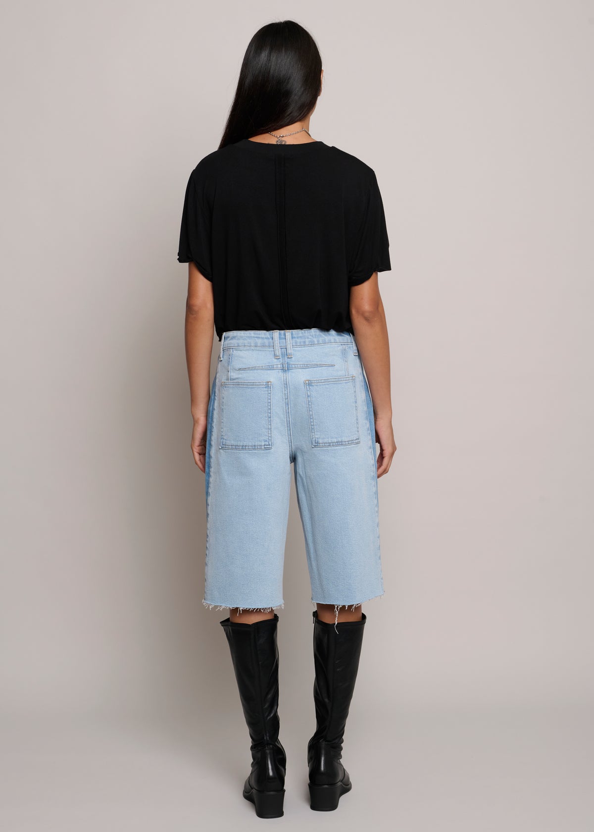 Person wearing a black t-shirt and light blue jeans with black knee-high boots on a plain background
