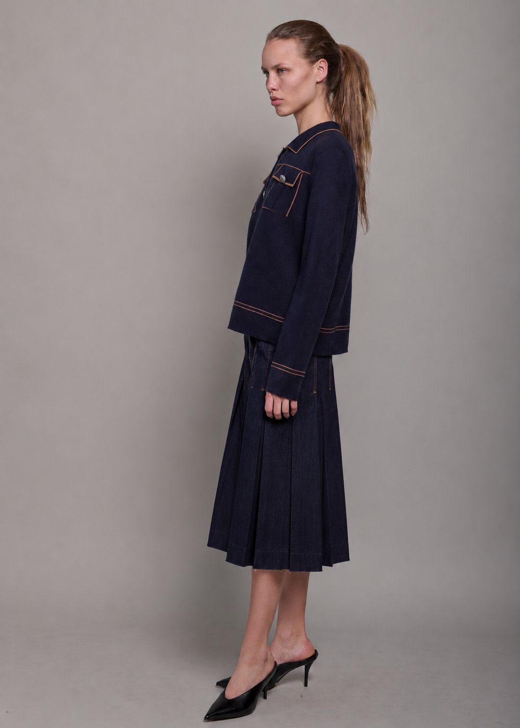 woman wearing a dark denim pleated midi skirt with a dark blue cashmere sweater. 