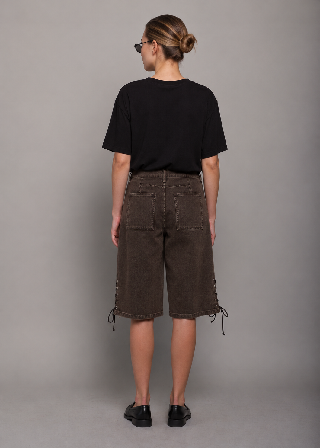 women wearing a black t-shirt and brown bermuda shorts with lace up detail. 